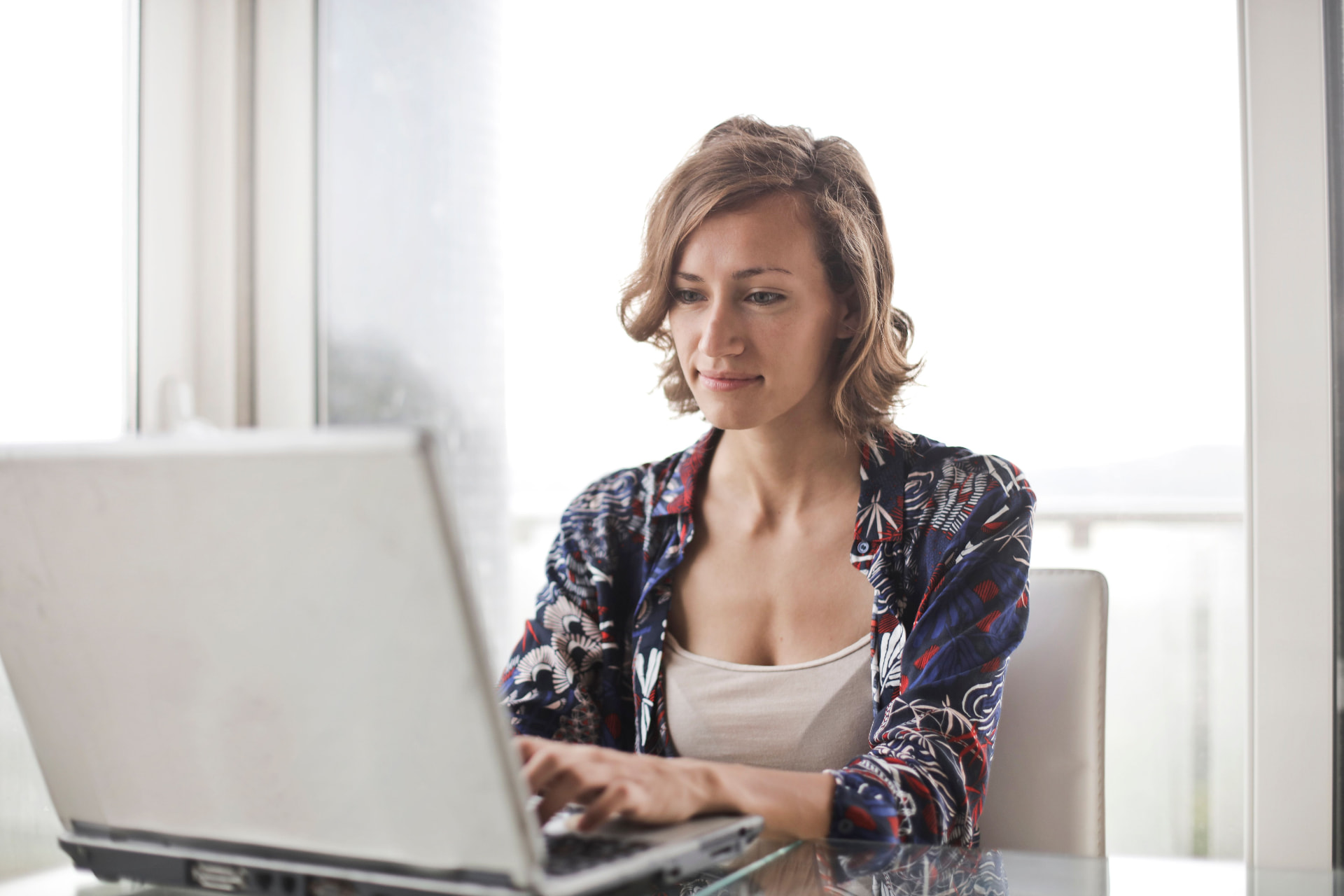 Small business owner researching AI search results and competitors on a laptop by a bright window